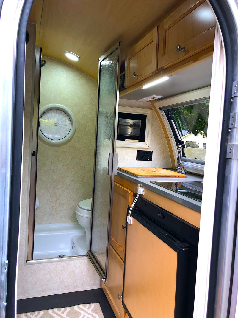 RV rental: Bright, compact camper interior featuring a kitchenette, wet bath with shower/toilet, & overhead storage. — photo 8