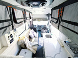 Discover this rv rental's interior: a clean kitchen, cozy lounge with pillows, and smart overhead storage in a camper van.