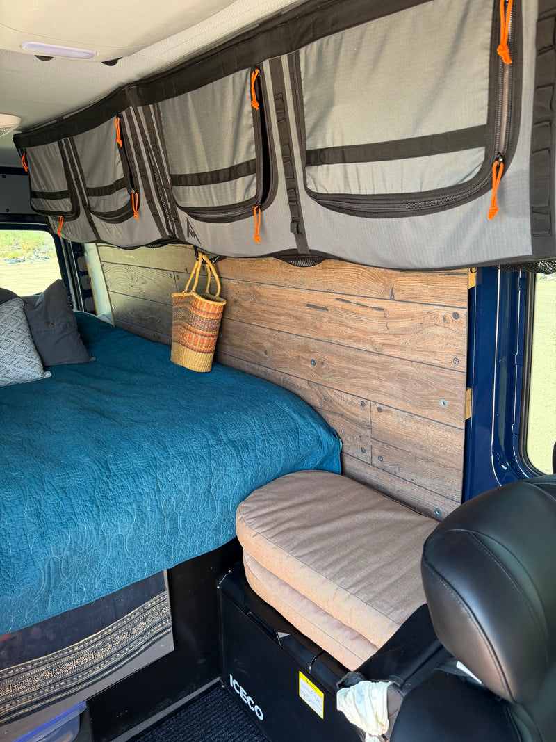 Cozy RV rental interior: a blue quilted bed, overhead storage, wooden paneling, and an Iceco cooler. Ideal campervan setup. — photo 15