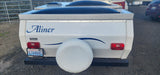 Rear view of a white Aliner pop-up camper for rv rental, displaying a Washington license plate and a rear-mounted spare tire.