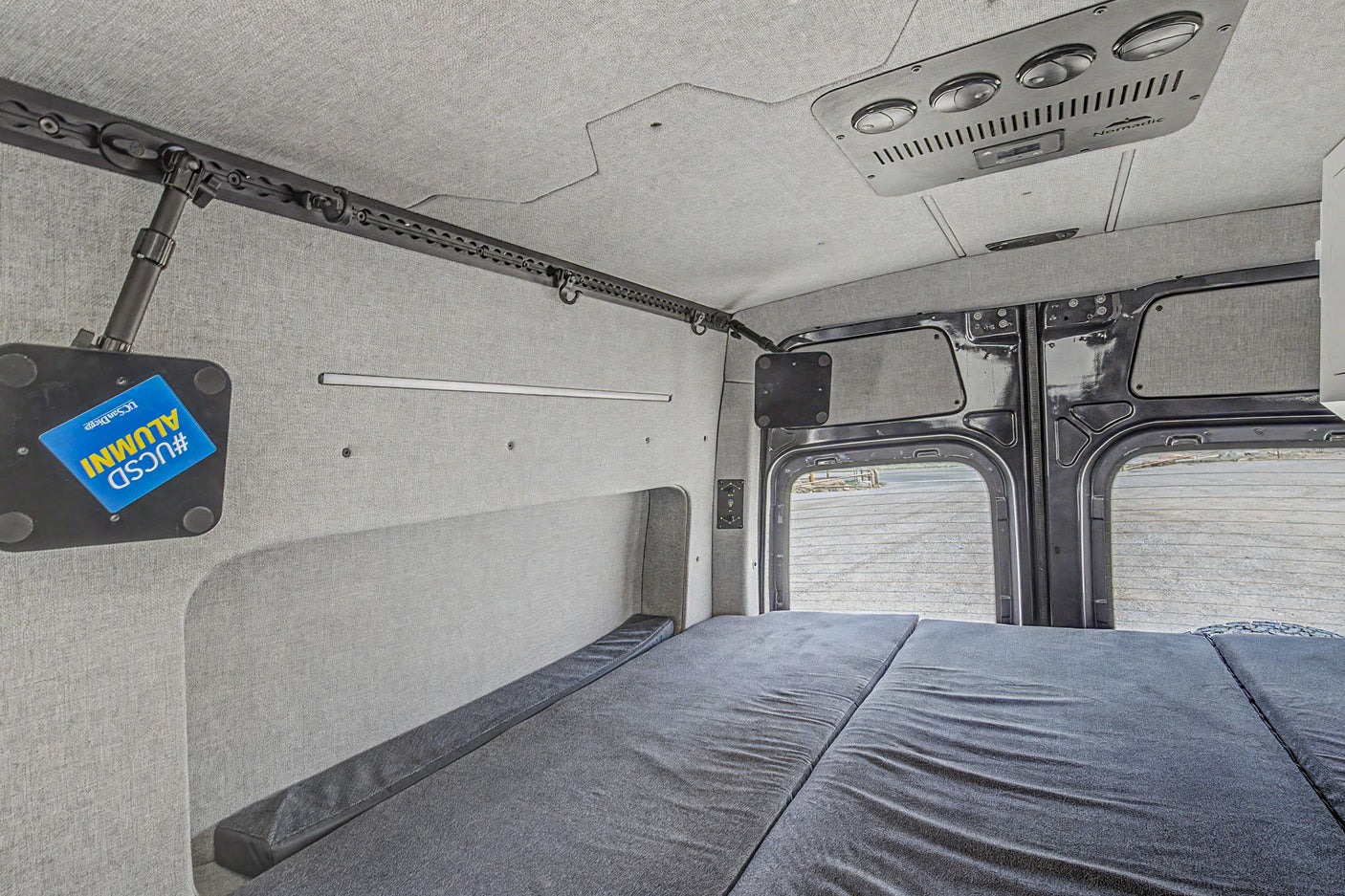 RV rental: Inside a modern camper van with a flexible bed setup, integrated storage track, and soft grey upholstery.
