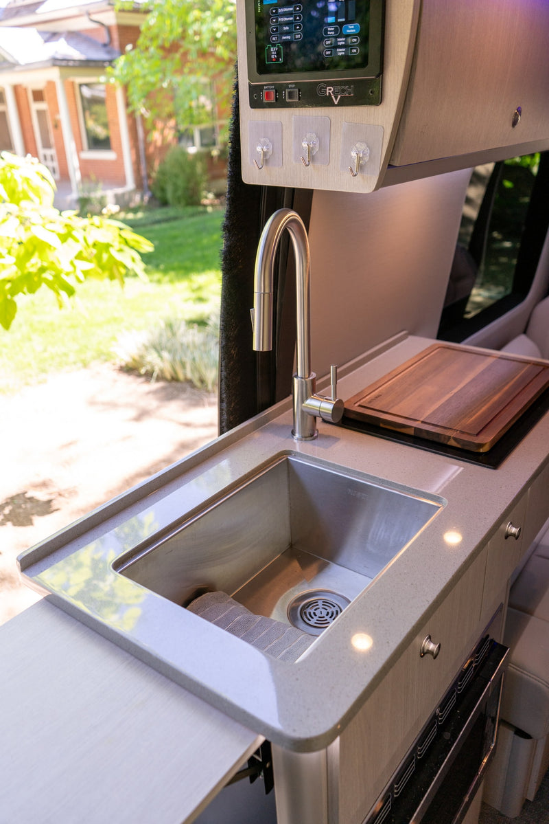 Modern RV rental kitchen with stainless steel sink, pull-out faucet, cutting board, and digital control panel. — photo 13