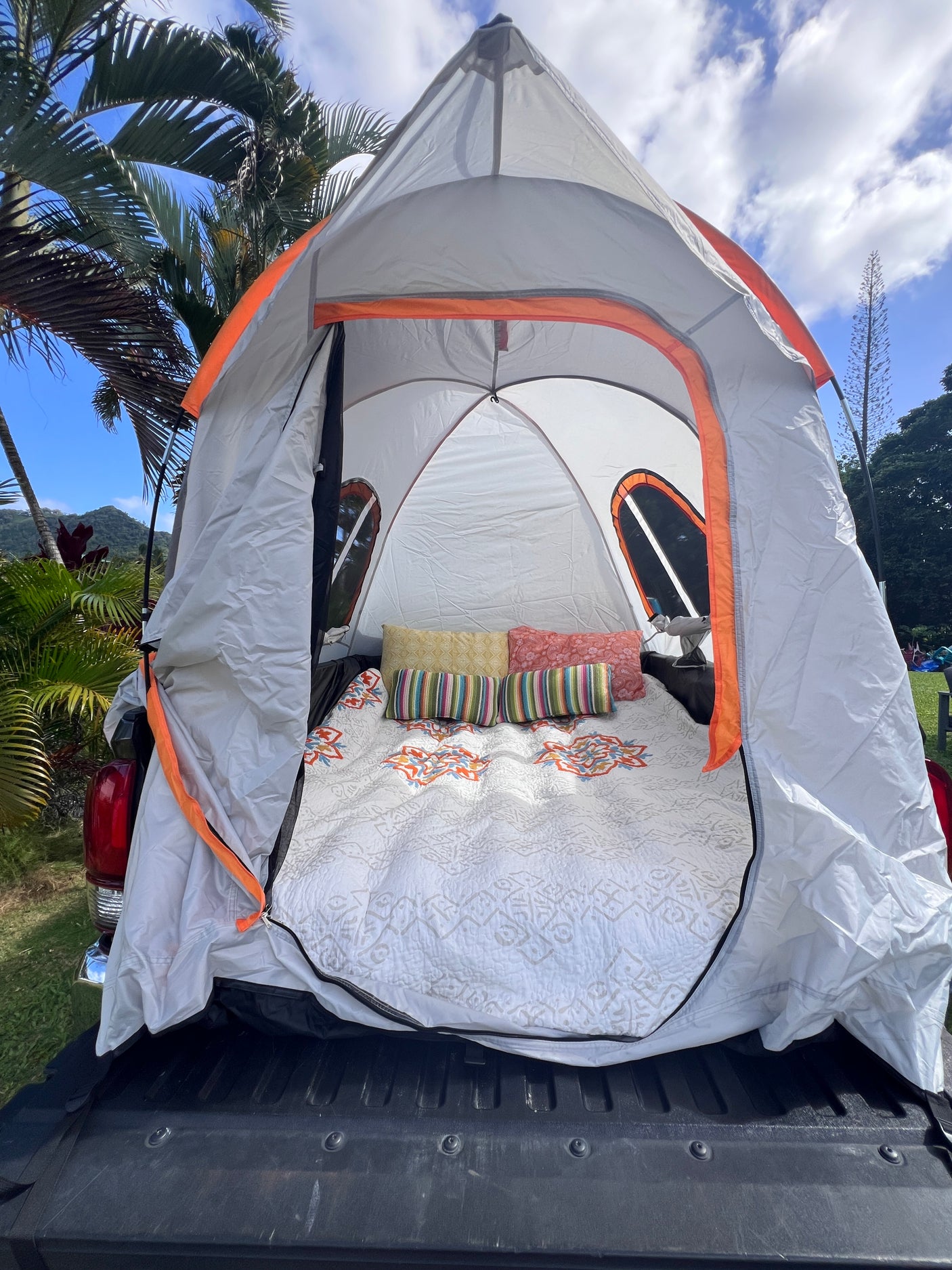 A cozy truck bed tent, an RV rental-like setup for camping adventures. White quilt, colorful pillows inside.