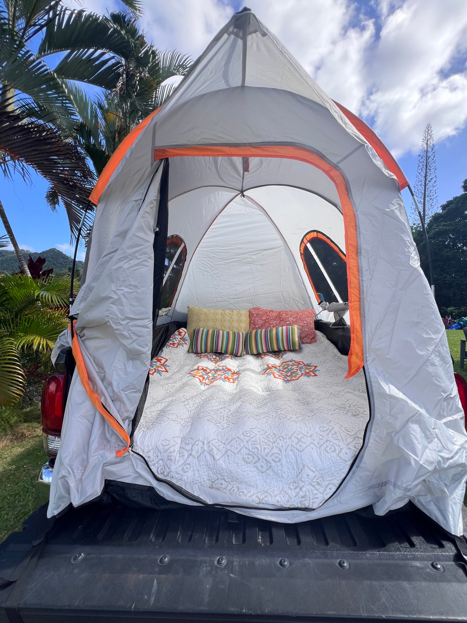 A cozy truck bed tent, an RV rental-like setup for camping adventures. White quilt, colorful pillows inside.
