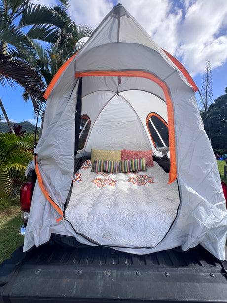 A cozy truck bed tent, an RV rental-like setup for camping adventures. White quilt, colorful pillows inside.