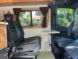 RV rental: Inside a comfortable camper van with black leather seating, a versatile table, and elegant wood paneling.