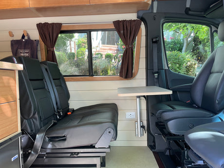 RV rental: Inside a comfortable camper van with black leather seating, a versatile table, and elegant wood paneling.