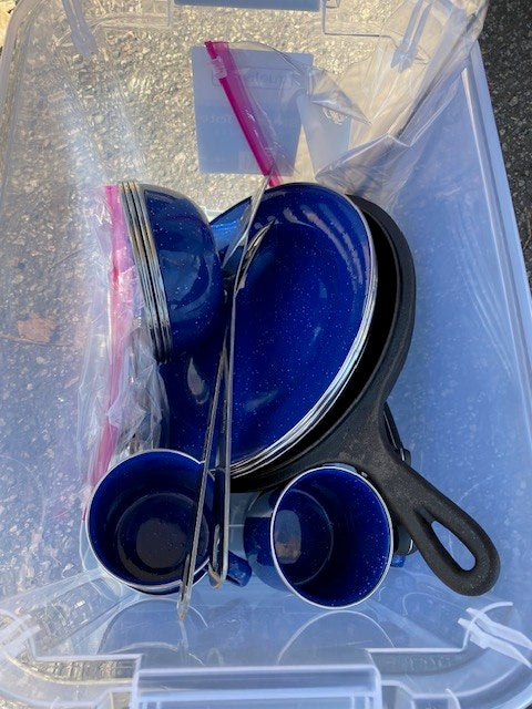 Essential RV rental camping kit: blue enamel dishes, cast iron pan, and tongs neatly stored for your adventure.