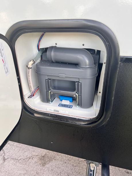 An open exterior compartment on an RV rental reveals its removable waste cassette tank for sanitary maintenance.