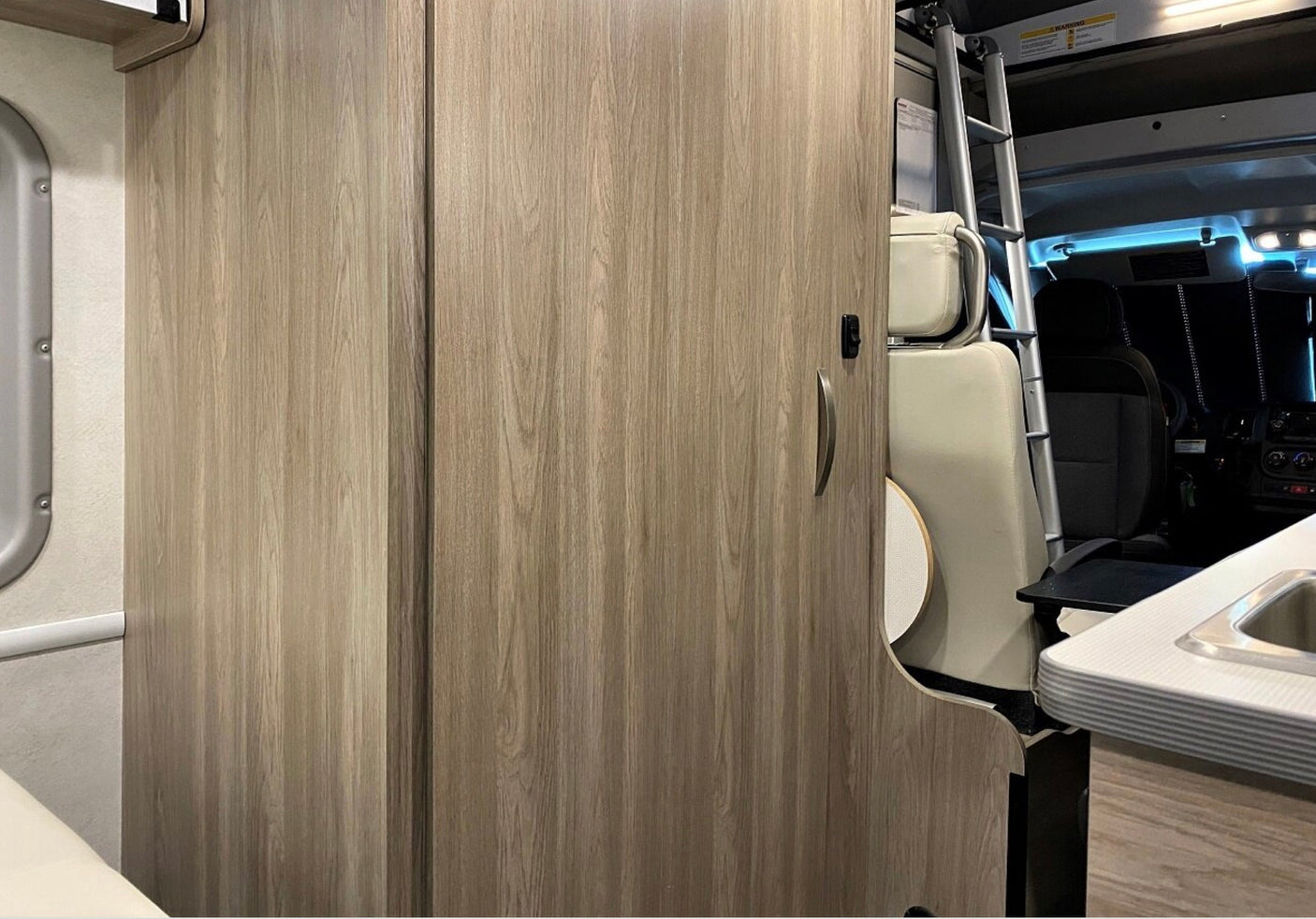 Inside an rv rental: light wood cabinets and a ladder to an upper bunk, with a kitchenette on the right. Functional compact living.