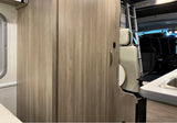 Inside an rv rental: light wood cabinets and a ladder to an upper bunk, with a kitchenette on the right. Functional compact living.