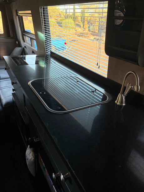 RV rental: Sleek black kitchen counter with a sink, stovetop, and desert view through window blinds.