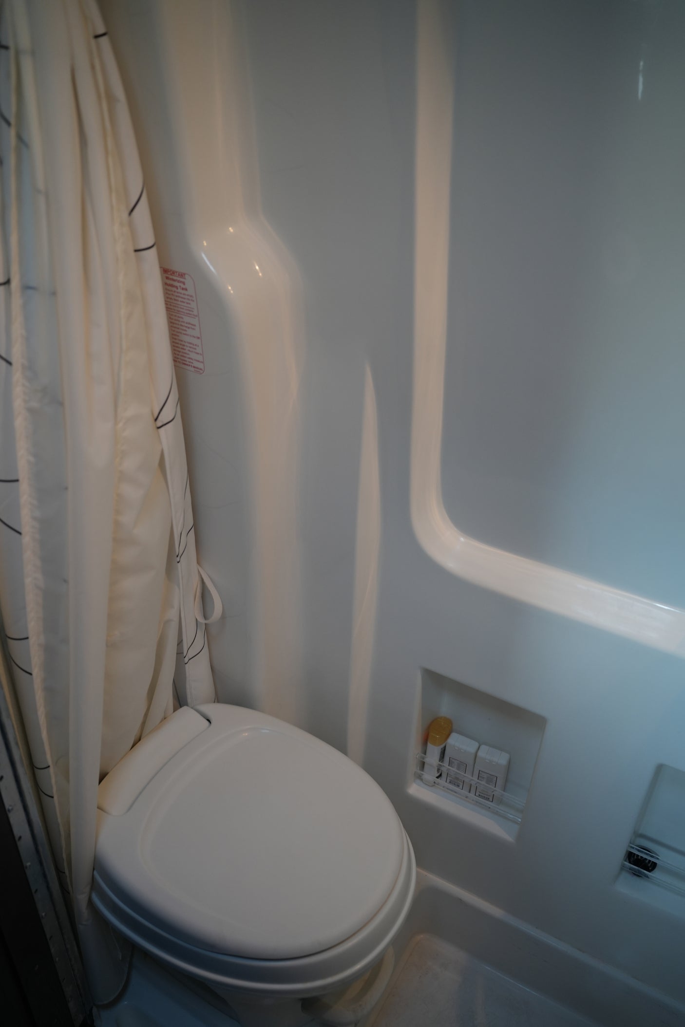 Inside an RV rental: a compact bathroom with a white toilet, shower curtain, and built-in storage for shower essentials.