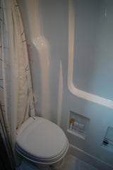Inside an RV rental: a compact bathroom with a white toilet, shower curtain, and built-in storage for shower essentials.