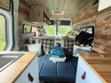 Cozy rv rental interior: wood-paneled walls, comfortable bed, compact kitchen, ideal for a scenic getaway.