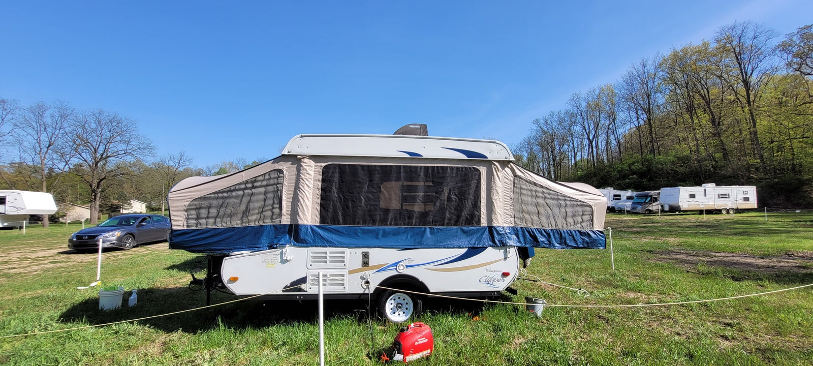  grassy campsite with bare trees against a blue sky.|An RV rental's pop-up camper interior