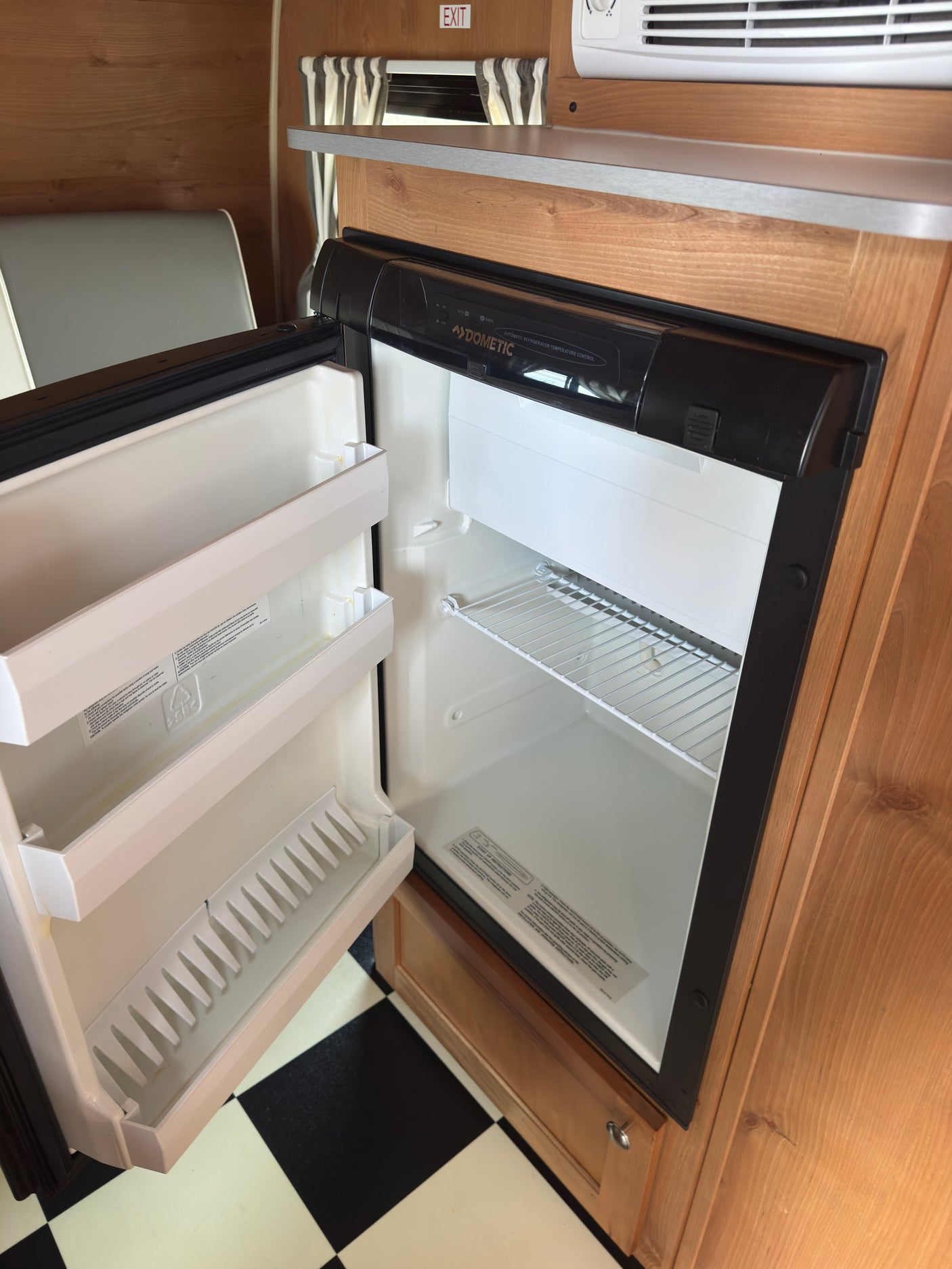 RV rental interior with an open, empty Dometic refrigerator, wood paneling, and checkered floor.