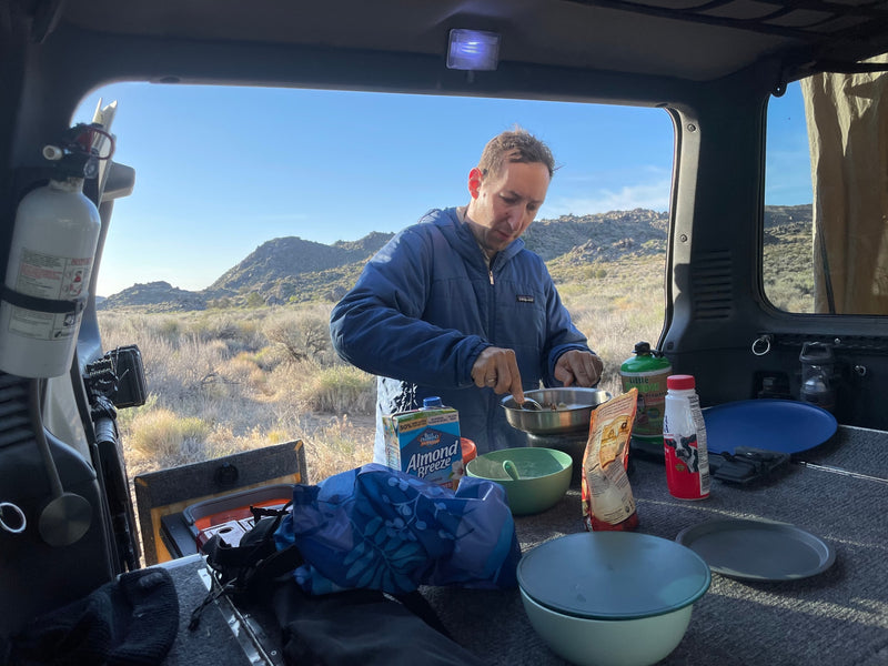 Cooking a meal in an RV rental, a man uses a portable stove and supplies like almond milk, surrounded by a desert landscape. — photo 6