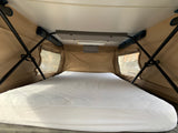 Inside an RV rental pop-top camper: A comfortable sleeping area with a white quilted mattress, beige fabric walls, and clear windows.