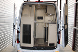 Rear interior of an RV rental camper van: kitchenette, sink, microwave, and separate room access.