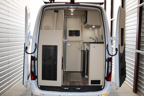 Rear interior of an RV rental camper van: kitchenette, sink, microwave, and separate room access.