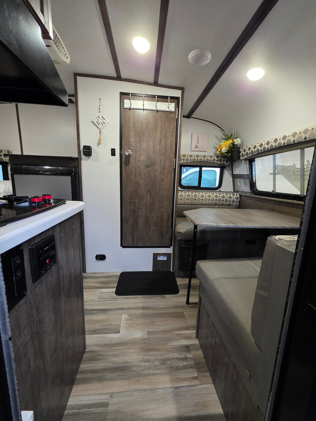 Modern RV rental interior with a functional kitchen, cozy dinette, and light wood flooring, ready for adventure.