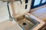 Compact kitchenette in an RV rental, featuring a stainless steel sink and chrome faucet. Ideal for travel and camping.