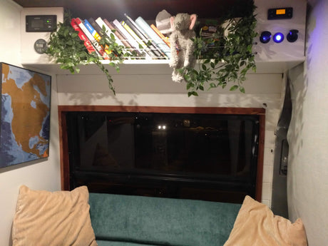 Cozy RV rental interior featuring a practical shelf with books, digital controls, map, and comfy seating.