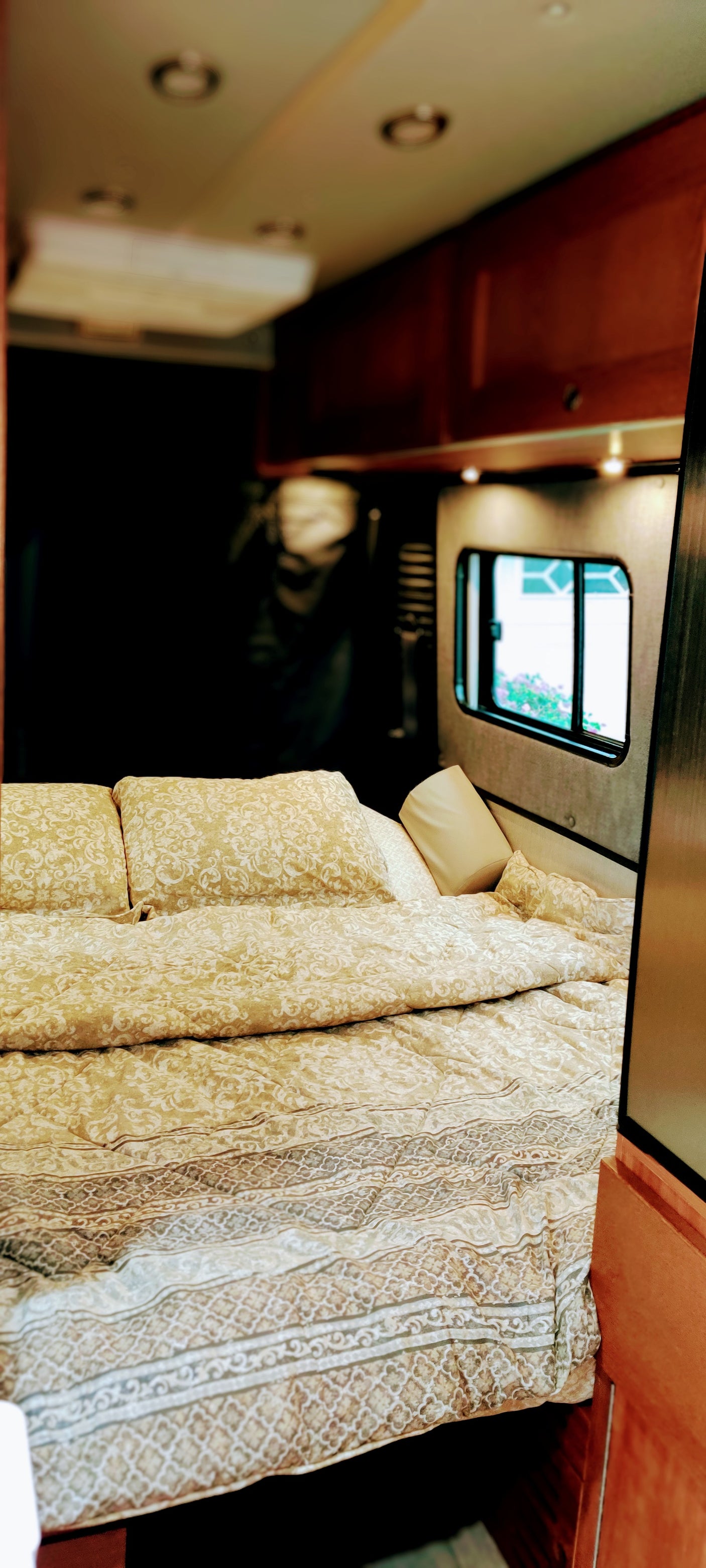 Comfortable RV rental bedroom featuring ornate gold bedding, plush pillows, and a window for natural light. Ideal for travel.