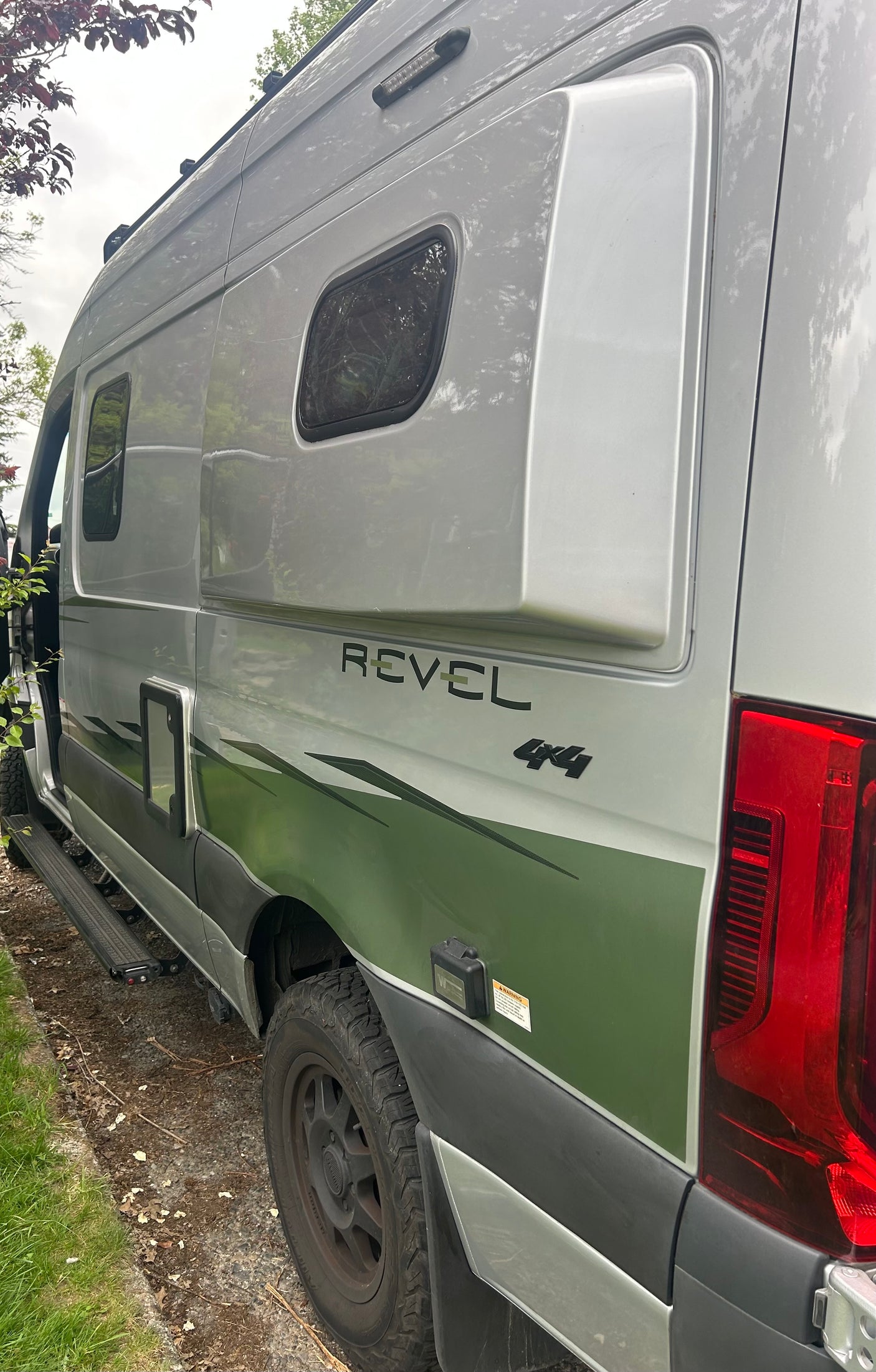 Explore in style! This silver Winnebago Revel 4x4 camper van, featuring a green graphic wrap, is ready for your next RV rental adventure.