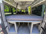 Interior of an RV rental camper van showing a raised bed with storage underneath, looking towards the front seats.