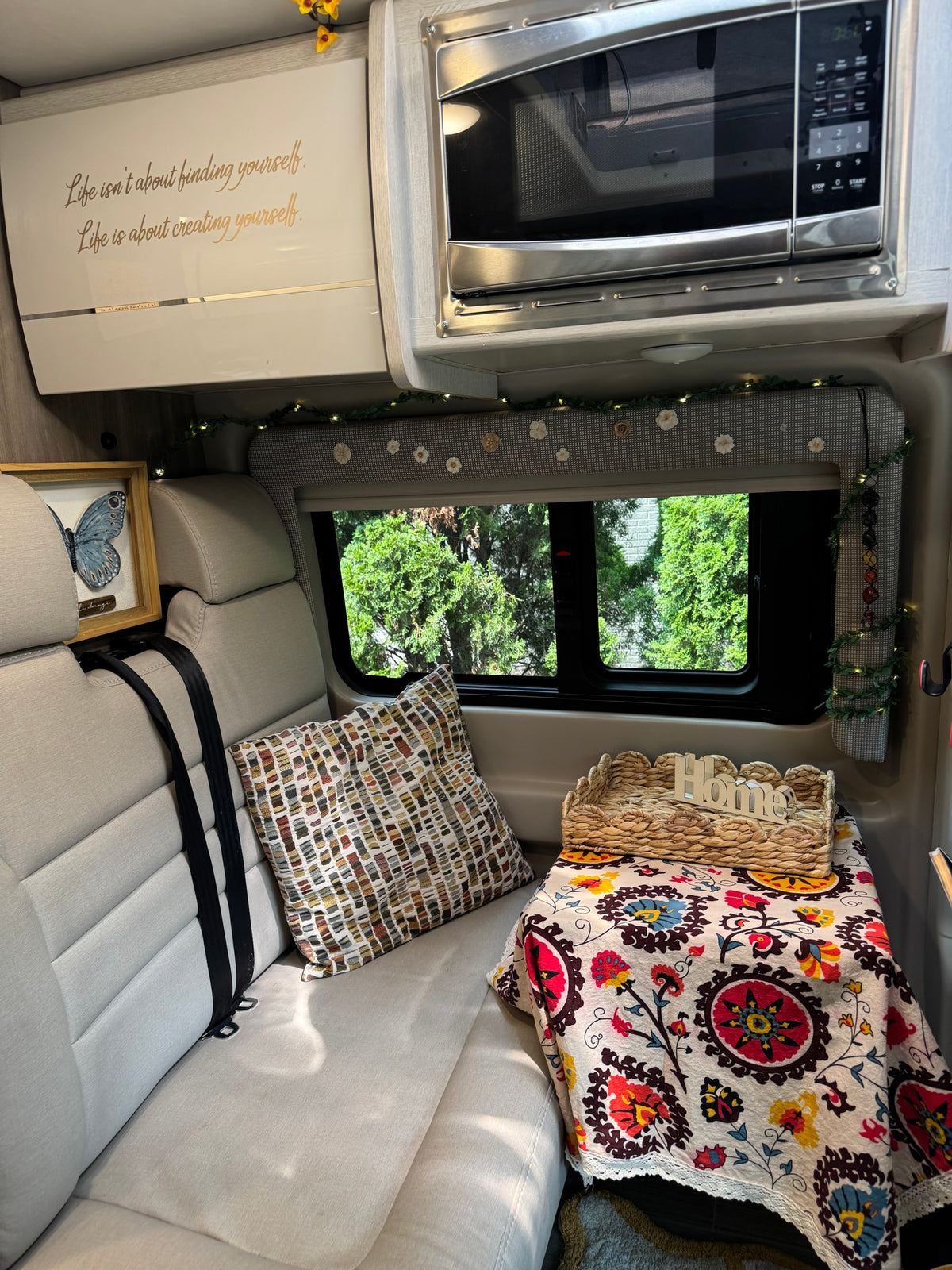 Inside a welcoming RV rental: comfy seating, microwave, colorful decor, and a window view of trees. — photo 7