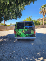 Rear of a custom green Ford van with a large hibiscus design, parked on a gravel lot. An ideal RV rental for a unique journey.