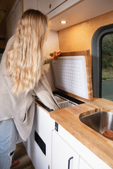 Inside an rv rental: A blonde woman opens a top-loading cooler in a stylish camper van kitchen setup.