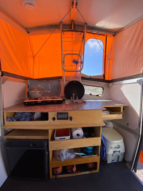 This RV rental camper interior features a compact kitchen (stove, sink), ample storage, a portable toilet, and a mini-fridge.