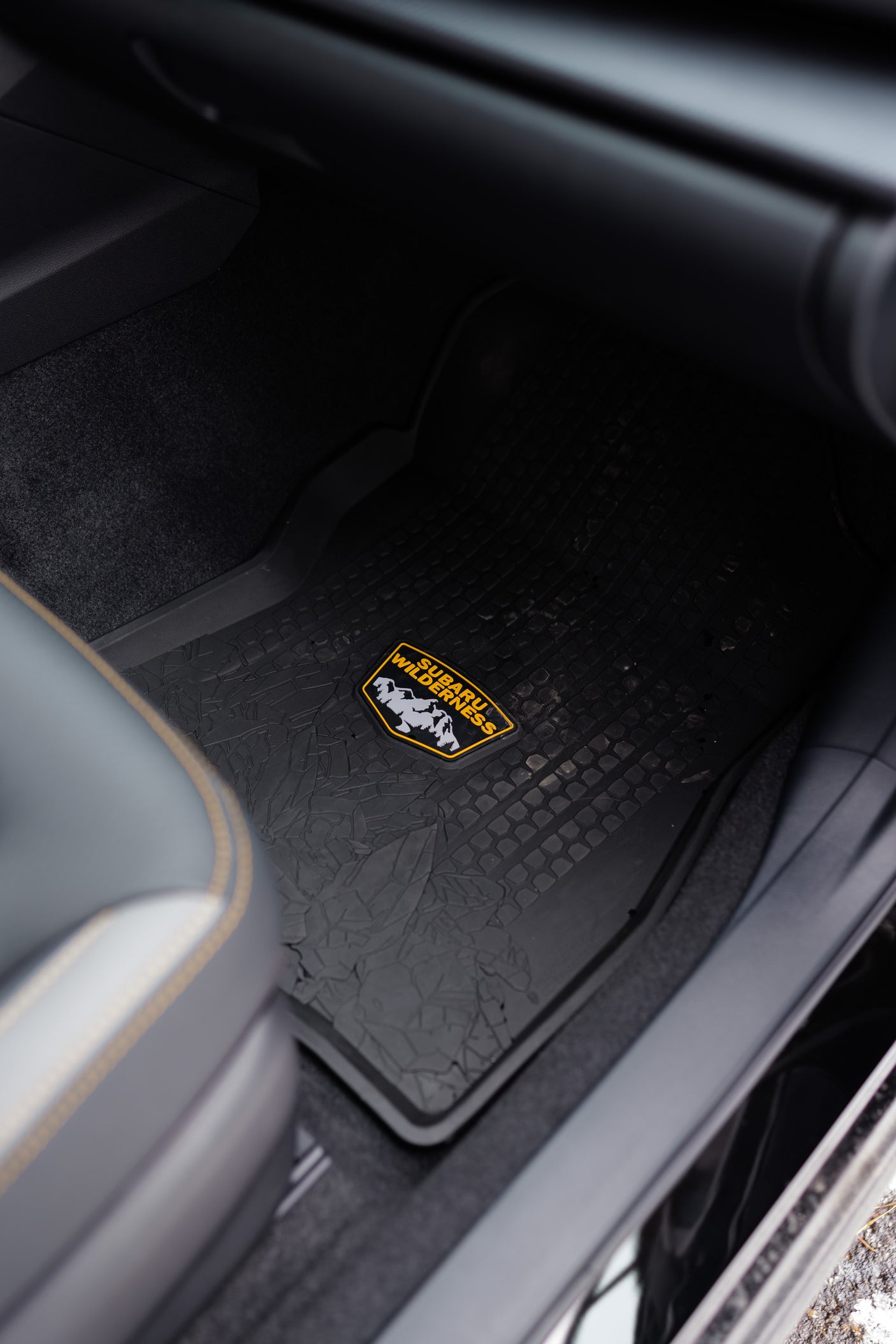 A black rubber floor mat for a Subaru Wilderness vehicle, featuring its yellow mountain logo. Great for adventures or complementing an RV rental.