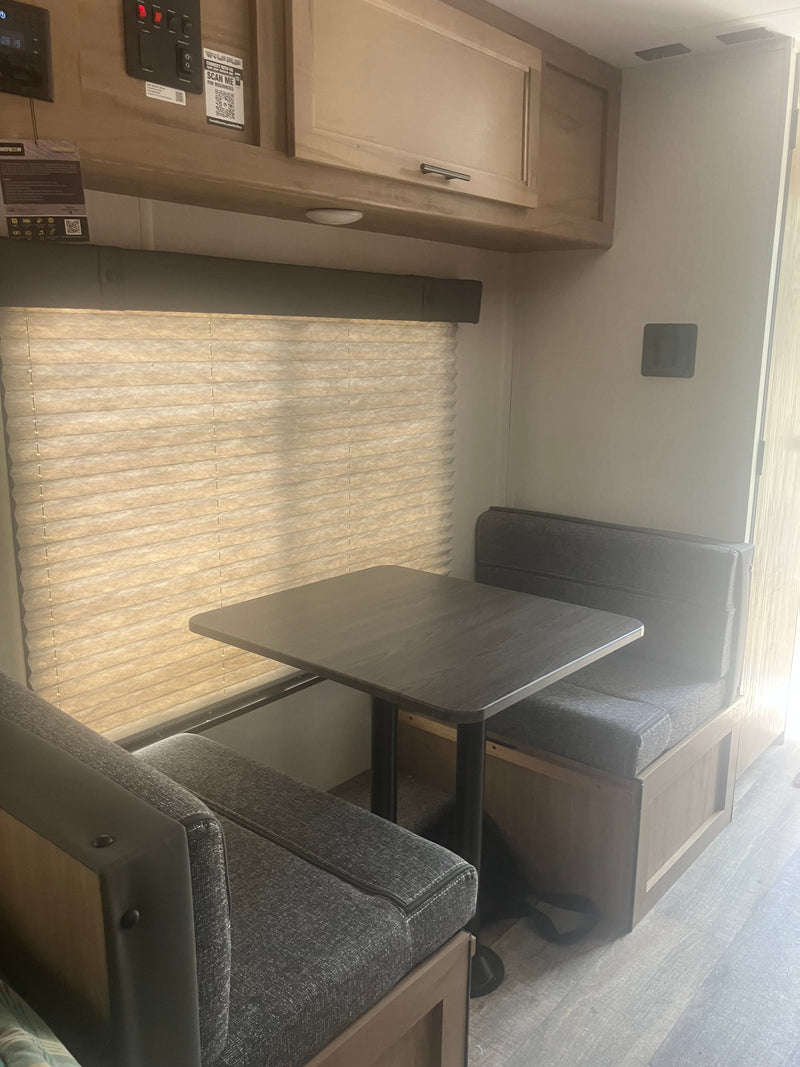 Step into your next rv rental adventure! This RV dinette features a dark table, grey upholstered benches, and a window with blinds. — photo 11