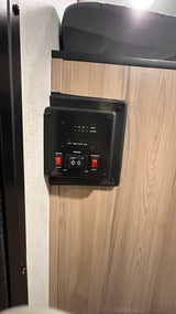 RV rental control panel displaying water pump, awning, exterior lights, and tank/battery levels on a wood-grain wall.