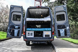 Rear view of custom rv rental van with open doors, revealing bunk beds, storage, and utility panel.