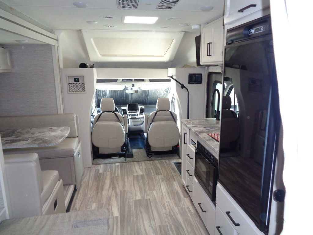Bright, modern RV rental interior: kitchen with microwave/fridge, dining booth, and front cockpit. Comfortable travel.