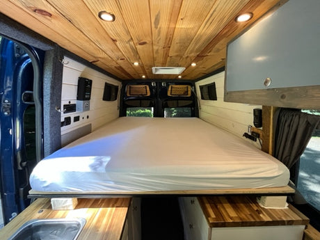 Explore this RV rental's cozy interior: wood ceiling, comfy bed, control panel, & sink. Ready for adventure!