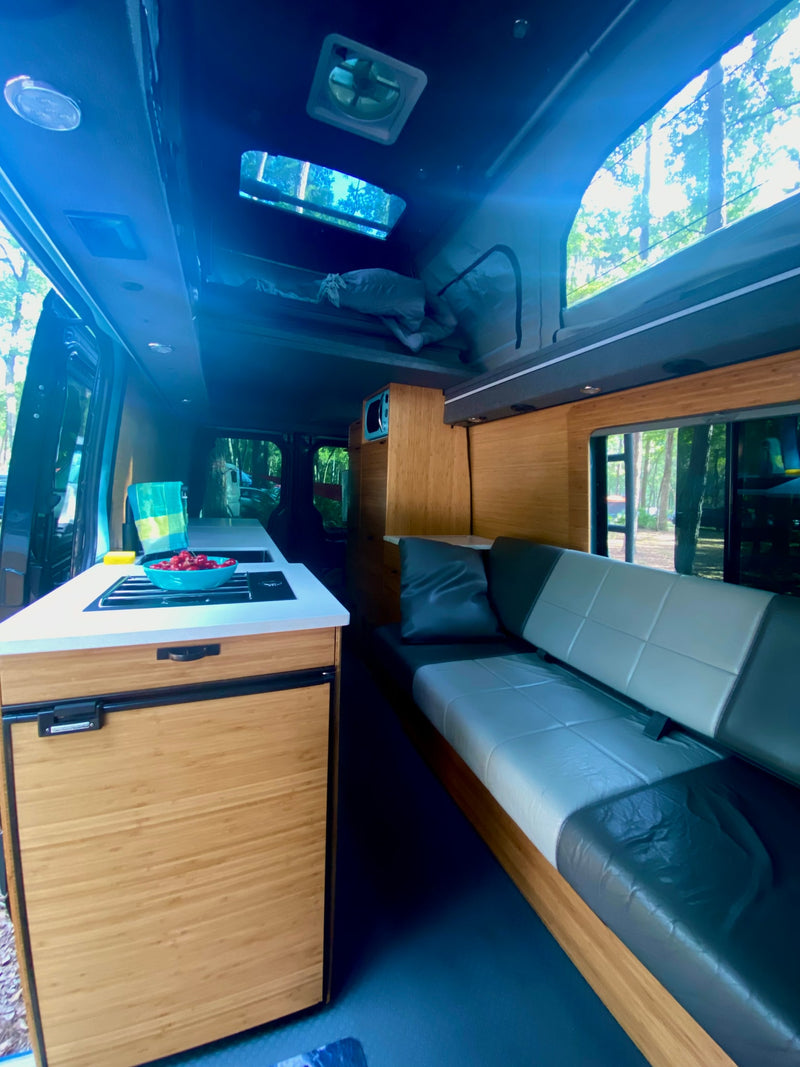 Modern RV rental interior: kitchenette with cherries, bamboo cabinetry, cozy sofa, and pop-top bed. — photo 11