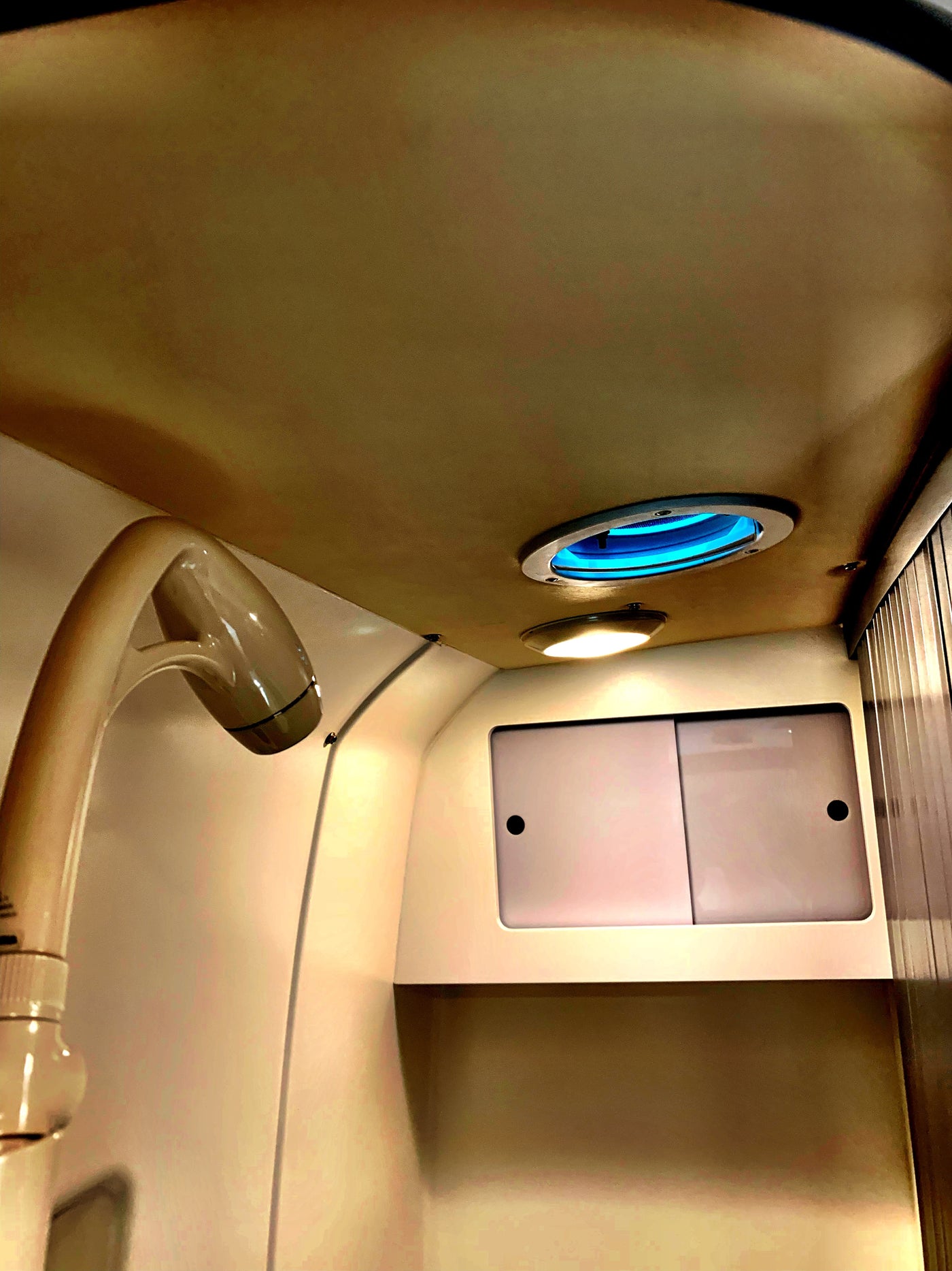 RV rental bathroom with a beige shower head, blue ceiling light, warm overhead light, and a two-door storage cabinet. — photo 17