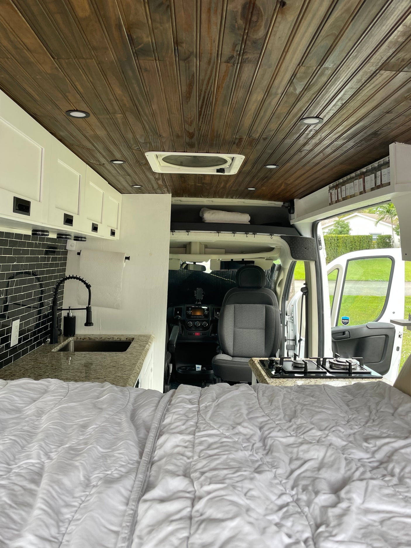 Modern RV rental: interior with cozy bed, kitchen area with black tile backsplash & sink, plus the driver's cabin.
