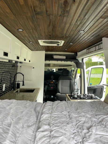 Modern RV rental: interior with cozy bed, kitchen area with black tile backsplash & sink, plus the driver's cabin.