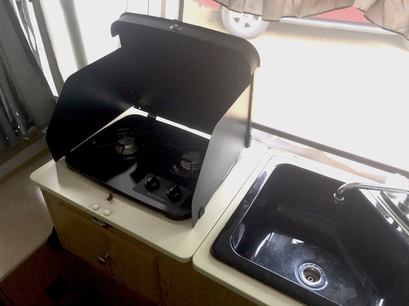 RV rental kitchen: compact black Suburban gas stove with open lid, alongside a matching sink. — photo 6