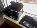 RV rental kitchen: compact black Suburban gas stove with open lid, alongside a matching sink.