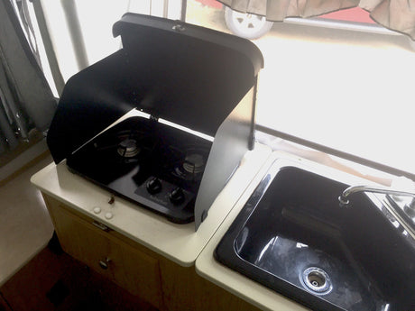 RV rental kitchen: compact black Suburban gas stove with open lid, alongside a matching sink.
