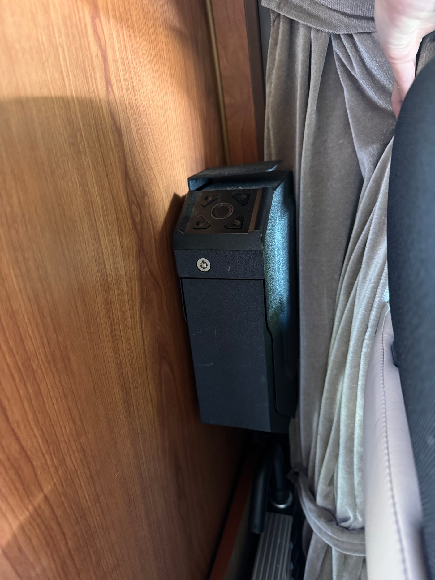 A small black security safe with a keypad and keyhole is mounted on wood paneling inside an RV rental.