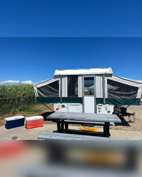Pop-up camper, picnic table, and coolers at a sunny campsite. Consider an RV rental for your next trip!